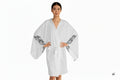 An AI Woman model wearing the moontiq white kimono robe 'I Got Wings' with feather designs on the flowing sleeves against a white background
